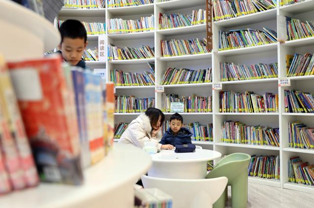 (260102) -- TIANJIN, Jan. 2, 2026 (Xinhua) -- A mother reads a book to her son at a library in the Jiefang North Road historical and cultural block in Tianjin, north China, Jan. 2, 2026. Located on the south bank of the Haihe River in Tianjin, the century-old Jiefang North Road historical and cultural block used to be a neighborhood where many banks clustered. Now, the streets there decorated with festive lights have attracted many tourists for a citywalk during the New Year's Day holiday. (Xinhua/Li Ran)
