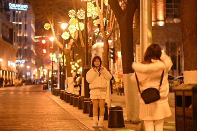 (260102) -- TIANJIN, Jan. 2, 2026 (Xinhua) -- A tourist poses for photos at the Jiefang North Road historical and cultural block in Tianjin, north China, Jan. 1, 2026. Located on the south bank of the Haihe River in Tianjin, the century-old Jiefang North Road historical and cultural block used to be a neighborhood where many banks clustered. Now, the streets there decorated with festive lights have attracted many tourists for a citywalk during the New Year's Day holiday. (Xinhua/Li Ran)
