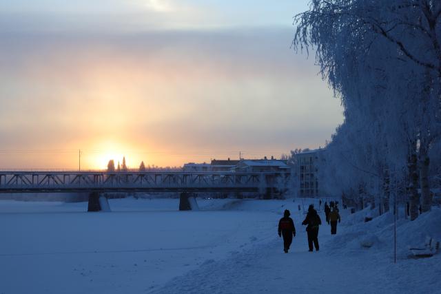 (260105) -- ROVANIEMI, Jan. 5, 2026 (Xinhua) -- People walk along the bank of the Kemijoki River in Rovaniemi, Finland, Jan. 3, 2026. Rovaniemi, a city located on the Arctic Circle, is renowned worldwide for aurora watching, winter sports, and reindeer sleigh rides. It is also well known internationally as the "home of Santa Claus," attracting large numbers of visitors from around the globe. (Xinhua/Zhu Haochen)