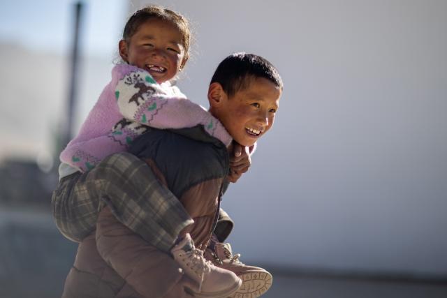 (260108) -- BEIJING, Jan. 8, 2026 (Xinhua) -- A boy with his sister on his back is pictured at a square in Zimgag Village of Chamco Township, in Dingri County of Xigaze City, southwest China's Xizang Autonomous Region, on Jan. 5, 2026. In January 2025, a 6.8-magnitude earthquake struck Dingri County in the city of Xigaze, leveling thousands of houses.
  Ten months after the earthquake, more than 32,500 destroyed or damaged houses have been restored and handed over to affected residents. 
   In Zimgag Village, one of the villages hardest hit by the earthquake, new houses are neat and sturdy, and supporting facilities are well-equipped. (Xinhua/Jiang Fan)