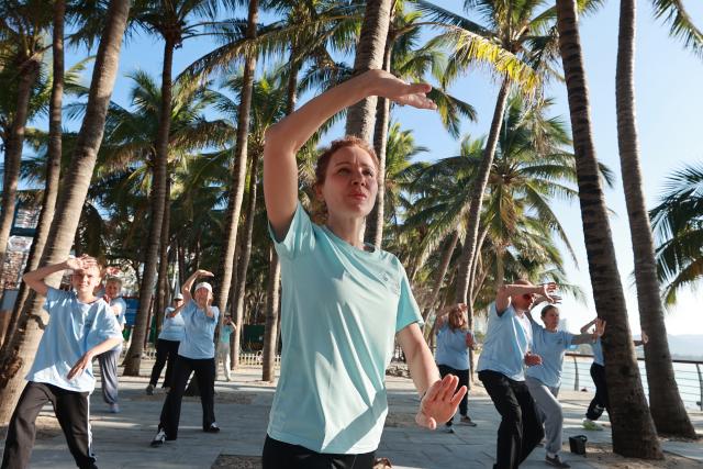(260110) -- SANYA, Jan. 10, 2026 (Xinhua) -- Foreign tourists learn Tai Chi under coconut groves at the Dadonghai scenic area in Sanya, south China's Hainan Province, Jan. 9, 2026. (Photo by Yuan Yongdong/Xinhua)
