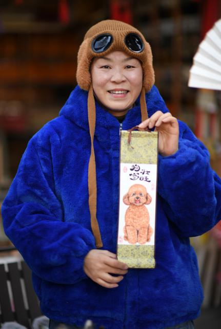 (260110) -- XI'AN, Jan. 10, 2026 (Xinhua) -- Artist Chen Lihua displays a pet dog portrait painted by herself in Shuyuanmen historical and cultural district in Xi'an, northwest China's Shaanxi Province, Jan. 9, 2026. Nestled near Beilin, meaning "the forest of stone steles" in Chinese, the Shuyuanmen historical and cultural district is a natural hub for Chinese calligraphy and painting arts. The district is now witnessing a rise in custom pet portrait services. Blending traditional artistic techniques with modern aesthetics, those offerings are winning the hearts of both pet lovers and tourists, bringing fresh and lively energy into this centuries-old neighborhood. (Xinhua/Li Yibo)