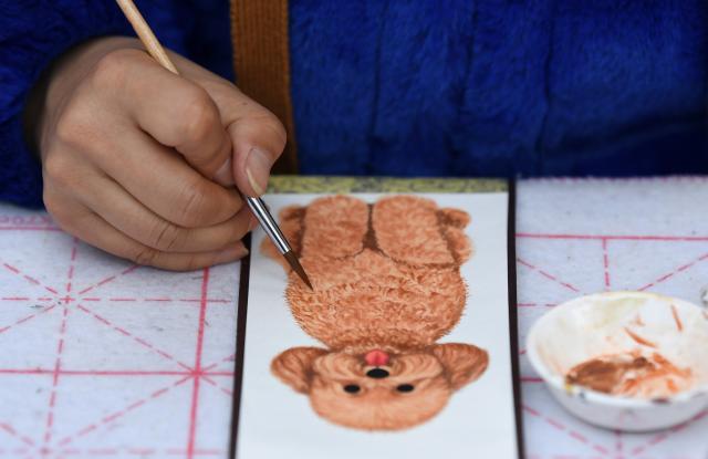 (260110) -- XI'AN, Jan. 10, 2026 (Xinhua) -- An artist paints a pet portrait in Shuyuanmen historical and cultural district in Xi'an, northwest China's Shaanxi Province, Jan. 9, 2026. Nestled near Beilin, meaning "the forest of stone steles" in Chinese, the Shuyuanmen historical and cultural district is a natural hub for Chinese calligraphy and painting arts. The district is now witnessing a rise in custom pet portrait services. Blending traditional artistic techniques with modern aesthetics, those offerings are winning the hearts of both pet lovers and tourists, bringing fresh and lively energy into this centuries-old neighborhood. (Xinhua/Li Yibo)