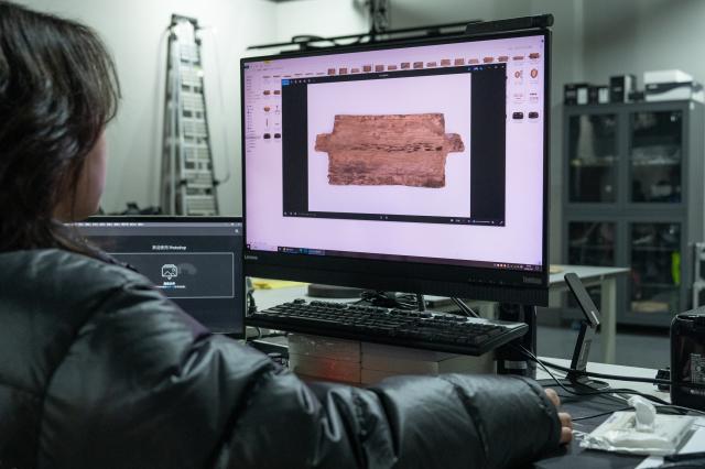 (260110) -- WUHAN, Jan. 10, 2026 (Xinhua) -- A staff member checks the photo of a cultural relic at the cultural relics protection center in Jingzhou, central China's Hubei Province, Jan. 9, 2026. Organic cultural relics represented by bamboo slips pose significant challenges in cultural relic preservation. In recent years, the cultural relics protection center in Jingzhou of Hubei Province has focused on innovation and application of preservation techniques for organic cultural relics, striving to ensure comprehensive care for such items. (Xinhua/Du Zixuan)