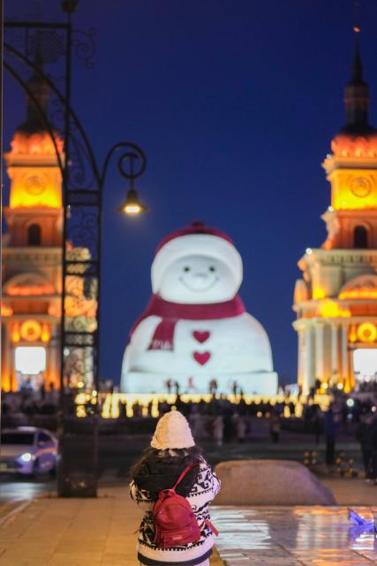 (260111) -- HARBIN, Jan. 11, 2026 (Xinhua) -- A tourist takes photos of the iconic giant snowman at the Qunli music park in Harbin, northeast China's Heilongjiang Province, Jan. 10, 2026.
  Standing 19 meters tall, measuring 14 meters in length and 11 meters in width, the snowman was dug and carved out of over 3,500 cubic meters of snow, with tourists swarming to take pictures of its classic red scarf and round face. (Xinhua/Wang Jianwei)