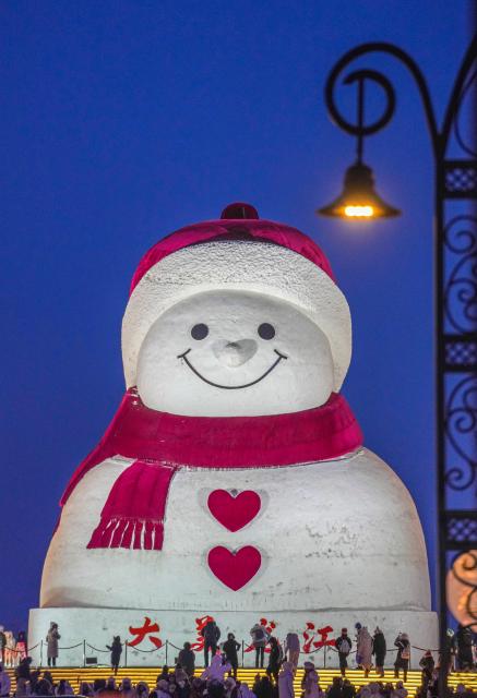 (260111) -- HARBIN, Jan. 11, 2026 (Xinhua) -- Tourists take photos of the iconic giant snowman at the Qunli music park in Harbin, northeast China's Heilongjiang Province, Jan. 10, 2026.
  Standing 19 meters tall, measuring 14 meters in length and 11 meters in width, the snowman was dug and carved out of over 3,500 cubic meters of snow, with tourists swarming to take pictures of its classic red scarf and round face. (Xinhua/Wang Jianwei)