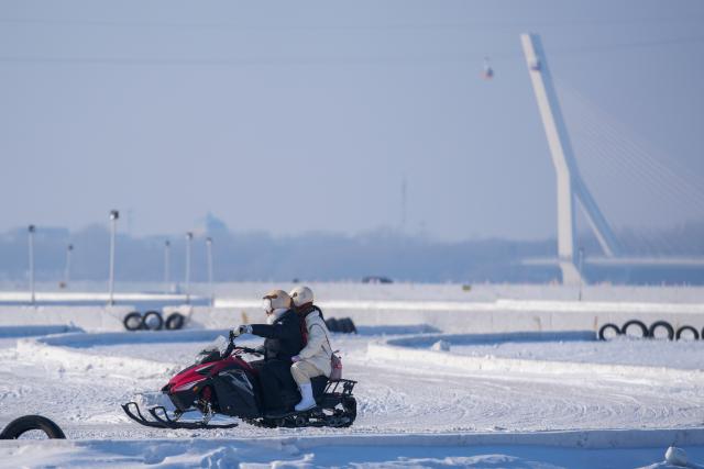 (260111) -- HARBIN, Jan. 11, 2026 (Xinhua) -- Tourists ride snow motorbike on the frozen surface of the Songhua River in Harbin, northeast China's Heilongjiang Province, Jan. 11, 2026. The surface of the Harbin section of Songhua River, now solidly frozen, serves as a "fun field," where locals and tourists alike enjoy themselves with ice-and-snow-themed amusements. (Xinhua/Wang Jianwei)