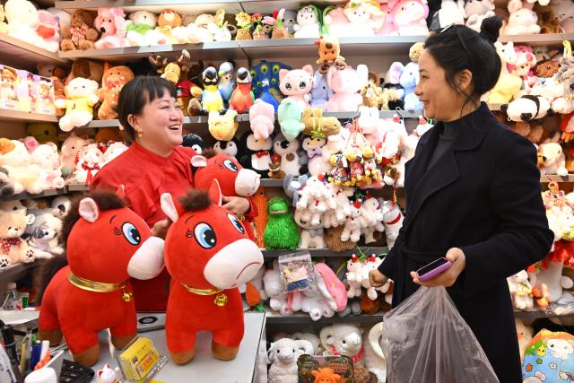 (260112) -- YIWU, Jan. 12, 2026 (Xinhua) -- A plush toy shop owner (L), with three "Cry-Cry Horse" stuffed toys in front of her, talks with a client at the Yiwu International Trade City in Yiwu, east China's Zhejiang Province, Jan. 12, 2026. A stuffed toy horse with a sullen face has gone viral recently on Chinese Internet. In Yiwu, a small commodities hub in east China, orders have soared as factories ramp up production to meet market demand. Dubbed "Cry-Cry Horse," the toy was originally a stitching mistake but unexpectedly touched the hearts of netizens with its pitiful expression which has a soothing effect. At present, nearly 20,000 of such toy horse are ordered every day. (Photo by Lyu Bin/Xinhua)