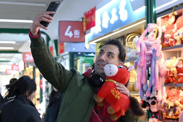 (260112) -- YIWU, Jan. 12, 2026 (Xinhua) -- A merchant from Finland poses for a selfie with a "Cry-Cry Horse" stuffed toy at the Yiwu International Trade City in Yiwu, east China's Zhejiang Province, Jan. 12, 2026. A stuffed toy horse with a sullen face has gone viral recently on Chinese Internet. In Yiwu, a small commodities hub in east China, orders have soared as factories ramp up production to meet market demand. Dubbed "Cry-Cry Horse," the toy was originally a stitching mistake but unexpectedly touched the hearts of netizens with its pitiful expression which has a soothing effect. At present, nearly 20,000 of such toy horse are ordered every day. (Photo by Lyu Bin/Xinhua)