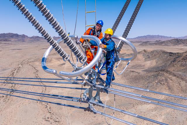 (260113) -- URUMQI, Jan. 13, 2026 (Xinhua) -- An aerial drone photo shows staff members checking cables of the Hami-Chongqing ±800 kV ultra-high voltage direct current transmission line, in Hami, northwest China's Xinjiang Uygur Autonomous Region, April 13, 2025. (Photo by Ma Yuan/Xinhua)