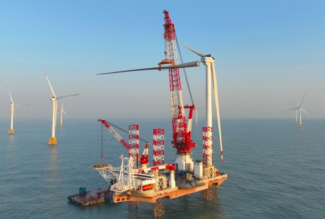 (260113) -- ZHANGZHOU, Jan. 13, 2026 (Xinhua) -- This drone photo taken on Jan. 13, 2026 shows one of the turbine blades being hoisted at the construction site of a 20-megawatt offshore wind turbine unit in the coastal waters of southeast China's Fujian Province. The wind turbine unit was successfully hoisted and installed here on Tuesday. (Xinhua/Lin Shanchuan)
