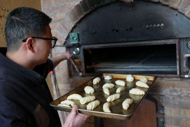 (260114) -- QUZHOU, Jan. 14, 2026 (Xinhua) -- A baker sends bread dough into an oven in Lulikeng Village of Changshan County, east China's Zhejiang Province, Jan. 14, 2026. Lulikeng Village has renovated its abandoned lime kilns into rural tourism facilities in recent years, turning the village into a destination for tourists from surrounding areas. Since 2024, various business sectors in the village have enabled over 150 villagers to find jobs right at their doorstep, and increased the village's income by more than 6 million yuan (about 0.86 million U.S. dollars). (Xinhua/Weng Xinyang)
