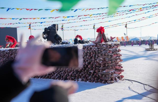 (260115) -- CHANGCHUN, Jan. 15, 2026 (Xinhua) -- This photo taken on Jan. 8, 2026 shows a tourist taking a photo of a wall made of fish during the opening ceremony of the 24th Chagan Lake Ice and Snow Fishing and Hunting Cultural Tourism Festival in Songyuan, northeast China's Jilin Province. (Xinhua/Yan Linyun)