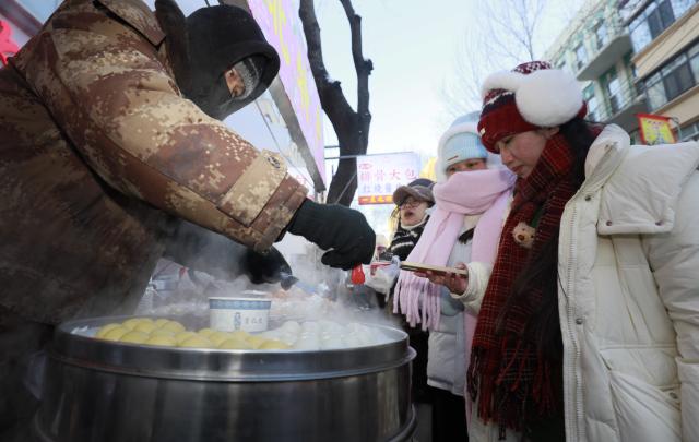 (260115) -- HARBIN, Jan. 15, 2026 (Xinhua) -- Tourists buy sticky steamed buns stuffed with bean paste at a morning market in Harbin, northeast China's Heilongjiang Province, Jan. 14, 2026. In winter, morning markets across Heilongjiang would open amid temperatures reaching minus 20 or even 30 degrees Celsius. Local residents and tourists stroll amid the stalls, where steam would rise among the cold air. (Photo by Zhang Shu/Xinhua)