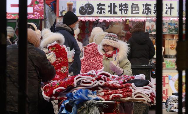 (260115) -- HARBIN, Jan. 15, 2026 (Xinhua) -- Tourists select vests with local characters at a morning market in Harbin, northeast China's Heilongjiang Province, Jan. 14, 2026. In winter, morning markets across Heilongjiang would open amid temperatures reaching minus 20 or even 30 degrees Celsius. Local residents and tourists stroll amid the stalls, where steam would rise among the cold air. (Photo by Zhang Shu/Xinhua)