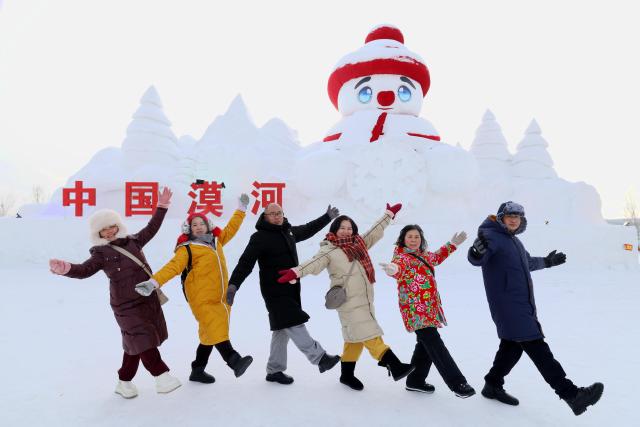 (260117) -- HARBIN, Jan. 17, 2026 (Xinhua) -- Tourists pose for photos in front of a giant snowman near the Mohe Railway Station in Mohe, northeast China's Heilongjiang Province, Jan. 16, 2026. With the arrival of the ice and snow season, various public facilities in Heilongjiang Province have created distinctive snowman-themed landscapes to attract locals and tourists. (Photo by Shao Tianli/Xinhua)