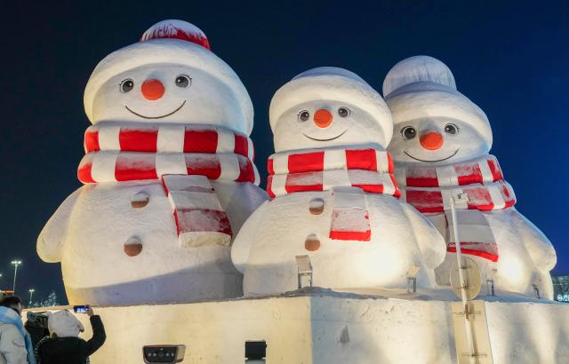 (260117) -- HARBIN, Jan. 17, 2026 (Xinhua) -- A tourist takes a photo of giant snowmen outside the Harbin Ice-Snow World in Harbin, northeast China's Heilongjiang Province, Jan. 13, 2026. With the arrival of the ice and snow season, various public facilities in Heilongjiang Province have created distinctive snowman-themed landscapes to attract locals and tourists. (Xinhua/Wang Jianwei)
