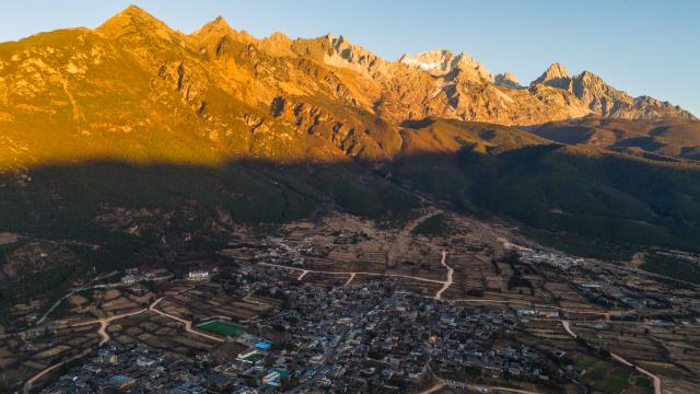 (260119) -- LIJIANG, Jan. 19, 2026 (Xinhua) -- A drone photo taken from Yuhu Village shows a sunrise view of Yulong Snow Mountain in Lijiang City, southwest China's Yunnan Province, Jan. 18, 2026. Yuhu Village, nestled in Baisha Township of Yulong Naxi Autonomous County in the city of Lijiang in Yunnan, is one of the earliest settlements of the Naxi ethnic people. The village was once among the poorest villages in Lijiang because of its poor soil and limited transportation links.   
  In recent years, Yuhu has developed a distinct path that balances economic growth with environmental protection. Leveraging its well-preserved Naxi cultural heritage and exceptional natural scenery, the village has attracted visitors from around the world. At the same time, it has continued to improve infrastructure and public services, attracting a growing number of residents to return home for businesses.  
  In 2025, Yuhu Village welcomed about 1.2 million visits, generating 75 million yuan (10.8 million U.S. dollars) in revenue -- with the average income of locals increasing from 13,000 yuan (1,865 U.S. dollars) in 2019 to about 35,000 yuan (5,022 U.S. dollars). (Xinhua/Gao Yongwei)