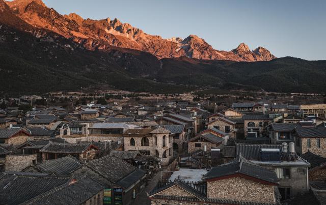 (260119) -- LIJIANG, Jan. 19, 2026 (Xinhua) -- A drone photo taken from Yuhu Village shows a sunrise view of Yulong Snow Mountain, in Lijiang City, southwest China's Yunnan Province, Jan. 18, 2026. Yuhu Village, nestled in Baisha Township of Yulong Naxi Autonomous County in the city of Lijiang in Yunnan, is one of the earliest settlements of the Naxi ethnic people. The village was once among the poorest villages in Lijiang because of its poor soil and limited transportation links.   
  In recent years, Yuhu has developed a distinct path that balances economic growth with environmental protection. Leveraging its well-preserved Naxi cultural heritage and exceptional natural scenery, the village has attracted visitors from around the world. At the same time, it has continued to improve infrastructure and public services, attracting a growing number of residents to return home for businesses.  
  In 2025, Yuhu Village welcomed about 1.2 million visits, generating 75 million yuan (10.8 million U.S. dollars) in revenue -- with the average income of locals increasing from 13,000 yuan (1,865 U.S. dollars) in 2019 to about 35,000 yuan (5,022 U.S. dollars). (Xinhua/Wang Guansen)