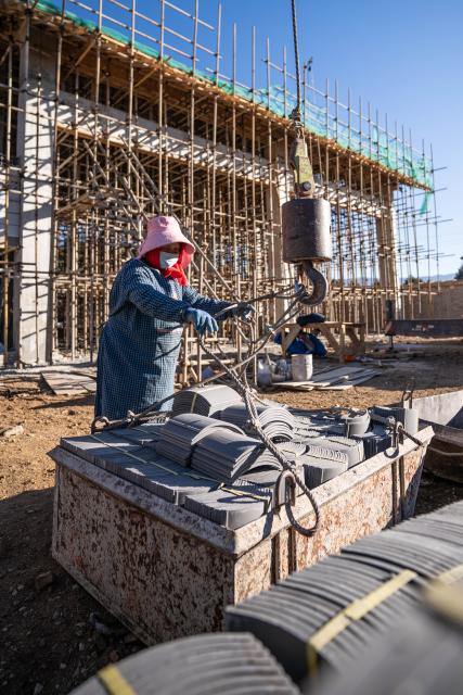 (260119) -- LIJIANG, Jan. 19, 2026 (Xinhua) -- A worker hooks tiles onto a crane at a construction site in Yuhu Village, Lijiang City, southwest China's Yunnan Province, Jan. 18, 2026. Yuhu Village, nestled in Baisha Township of Yulong Naxi Autonomous County in the city of Lijiang in Yunnan, is one of the earliest settlements of the Naxi ethnic people. The village was once among the poorest villages in Lijiang because of its poor soil and limited transportation links.   
  In recent years, Yuhu has developed a distinct path that balances economic growth with environmental protection. Leveraging its well-preserved Naxi cultural heritage and exceptional natural scenery, the village has attracted visitors from around the world. At the same time, it has continued to improve infrastructure and public services, attracting a growing number of residents to return home for businesses.  
  In 2025, Yuhu Village welcomed about 1.2 million visits, generating 75 million yuan (10.8 million U.S. dollars) in revenue -- with the average income of locals increasing from 13,000 yuan (1,865 U.S. dollars) in 2019 to about 35,000 yuan (5,022 U.S. dollars). (Xinhua/Gao Yongwei)