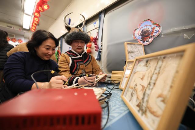 (260119) -- HARBIN, Jan. 19, 2026 (Xinhua) -- A tourist from Malaysia (L) experiences painting techniques of Elunchun nationality on K7041, a train themed on folk culture of northeast China, in northeast China's Heilongjiang Province, Jan. 19, 2026. Recently, tourists from Southeast Asian countries have been flocking to Harbin, hailed as China's "Ice City," with unprecedented enthusiasm. (Photo by Xu Shuai/Xinhua)