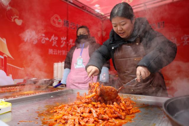 (260120) -- DINGXI, Jan. 20, 2026 (Xinhua) -- A vendor prepares local cuisine at her stall at a Spring Festival shopping market in Anding District of Dingxi City, northwest China's Gansu Province, Jan. 19, 2026. The Spring Festival shopping market opened its doors at the potato trading center in Anding District of Dingxi City on Monday and will run until Chinese Lunar New Year's Eve. 
   The marketplace drew tens of thousands of visitors on the opening day, with agricultural specialties, local delicacies, children's entertainment, Qinqiang opera performances, and intangible cultural heritage experiences. There were also hundreds of social media influencers broadcasting the bustling market via live-streaming, and collaborating with on-site vendors to promote local high-quality agricultural products, in an effort to activate holiday consumption potential. (Xinhua/Chen Bin)