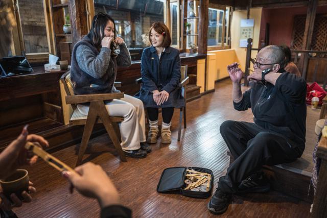 (260121) -- LIJIANG, Jan. 21, 2026 (Xinhua) -- He Dehua (R) performs the Chinese mouth harp for customers at the "Wayfarers" music club at the ancient city of Lijiang, southwest China's Yunnan Province, Jan. 16, 2026. He Dehua, 51, and his wife refurbished an old house of theirs in October 2025, and turned it into a music club called "Wayfarers," where they can share their personal stories with travelers and long-lost friends.
   The name "Wayfarers" came from a CD He had co-produced, drawing inspiration from his memory of watching elders of the family leaving hometown to work for livelihood. "We are all wayfarers in our own life, but we must not forget to search for the truth of life and the true self," said He.
   He has been a career musician for about three decades since he went to learn guitar playing in Beijing in 1997. Back to his hometown in Lijiang, he started to challenge himself by impressing the visitors to this olden city with music, songs and sounds of nature.
   He set out to collect voices and sounds in 2011, and has garnered more than 200 hours of recordings, which included some intangible cultural heritage items, voices in routine life, and melodies performed by folk artists. (Xinhua/Wang Guansen)