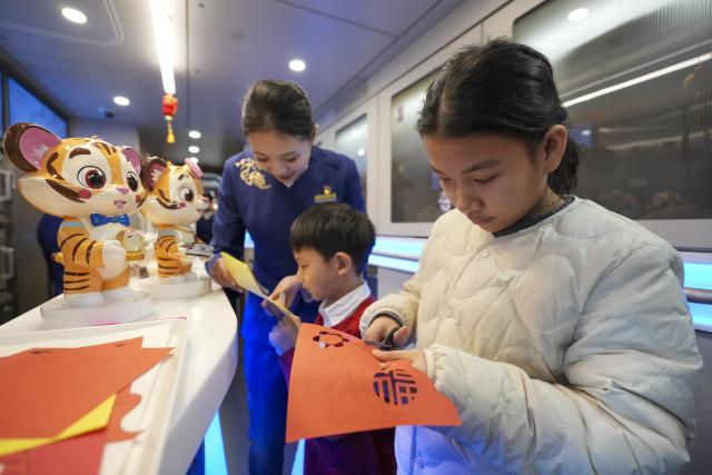 (260122) -- HARBIN, Jan. 22, 2026 (Xinhua) -- Children experience paper-cutting on bullet train G902 from Harbin, northeast China's Heilongjiang Province, to Beijing, capital of China, on Jan. 22, 2026. The Beijing-Harbin high-speed railway marked the 5th anniversary of its full operation on Thursday. At 1,198 kilometers, the rail line links China's northeastern provinces of Liaoning, Jilin and Heilongjiang with the capital Beijing. (Xinhua/Wang Song)