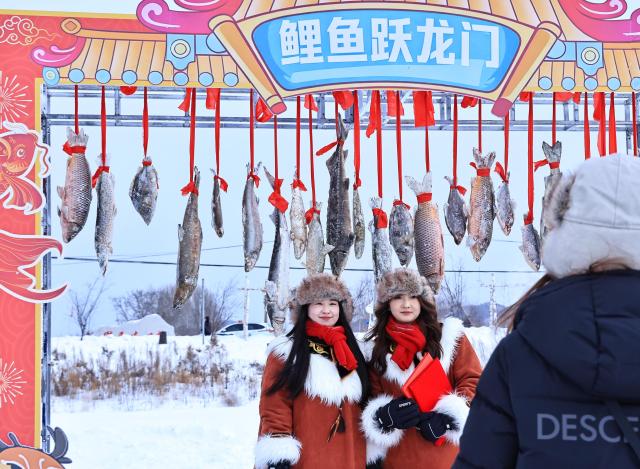 (260123) -- TONGJIANG, Jan. 23, 2026 (Xinhua) -- Tourists pose for photos during a winter fishing festival in Jiejinkou Hezhe Ethnic Township, Tongjiang City, northeast China's Heilongjiang Province, on Jan. 23, 2026. The event, held on a frozen lake, is part of the province's winter fishing events. It integrates traditional Hezhe fishing and hunting culture with folk sports, offering visitors an immersive experience of the icy landscape and unique Hezhe customs. (Photo by Liu Wanping/Xinhua)