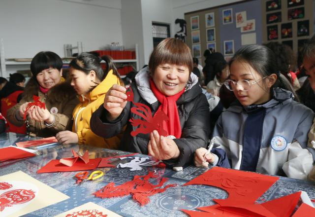 (260123) -- BEIJING, Jan. 23, 2026 (Xinhua) -- An inheritor of paper-cutting art, an intangible cultural heritage, guides a student during a paper-cutting event in Ruyang County, Luoyang City of central China's Henan Province, Jan. 23, 2026. Chinese people are busy preparing fresh flowers, Chinese knots, spring couplets, and other traditional necessities to celebrate the upcoming Spring Festival, or the Chinese New Year. (Photo by Kang Hongjun/Xinhua)