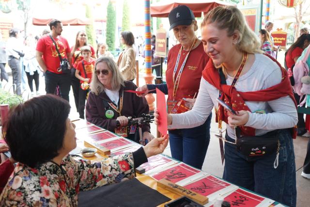 (260124) -- ANAHEIM, Jan. 24, 2026 (Xinhua) -- A calligrapher shows a Chinese character to visitors during the Lunar New Year celebrations at Disney California Adventure Park in Anaheim, California, the United States, Jan. 23, 2026. Disneyland Resort kicked off its annual Lunar New Year celebrations on Friday, transforming the park into a vibrant showcase of Asian cultures, cuisine and traditions that continues to attract growing interest from U.S. visitors.
   TO GO WITH "Feature: Disneyland's Lunar New Year celebrations offer immersive window into Asian cultures" (Photo by Zeng Hui/Xinhua)