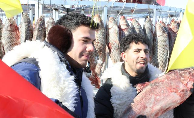 (260124) -- SHENYANG, Jan. 24, 2026 (Xinhua) -- Foreign tourists pose for photos with newly-caught fish at Wolong Lake in Kangping County of Shenyang, northeast China's Liaoning Province, Jan. 24, 2026. A winter fishing event began here on Saturday, featuring performances, fish cuisine, and ice and snow recreational facilities. (Xinhua/Han He)