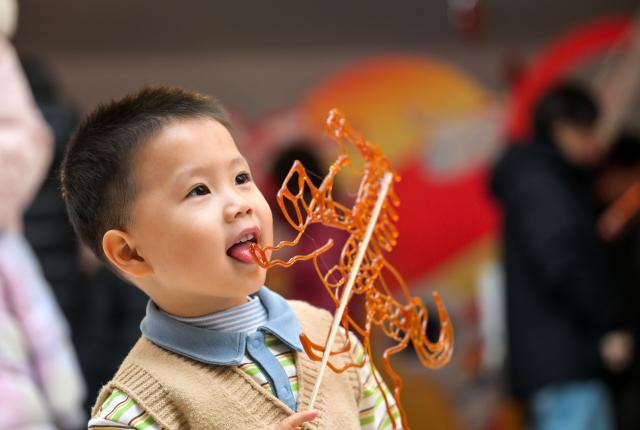 (260125) -- BEIJING, Jan. 25, 2026 (Xinhua) -- A child tastes a sugar painting during a temple fair for children in north China's Tianjin, on Jan. 24, 2026. A special temple fair tailored for children kicked off in north China's Tianjin on Saturday. Crowds of parents and kids gathered at the fair to experience the festive atmosphere ahead of the Spring Festival. The event features a variety of activities including traditional handicraft making, Tianjin-style food tasting, and interactive games. (Xinhua/Zhao Zishuo)