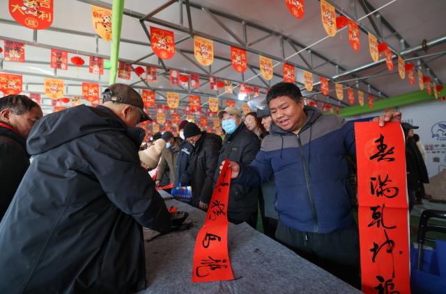 (260126) -- TIANJIN, Jan. 26, 2026 (Xinhua) -- People collect New Year couplets at an open air market during the Laba Festival in Tianjin, north China, Jan. 26, 2026. This year's Laba Festival falls on Monday, coinciding with the opening of the Lutai Market in Tianjin. The market features traditional activities such as free distribution of Laba porridge, calligraphy of the character "Fu" for blessings, and a village chef competition, attracting numerous residents from surrounding areas. (Xinhua/Sun Fanyue)