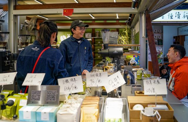 (260127) -- KUNMING, Jan. 27, 2026 (Xinhua) -- A barista (2nd L) talks with a tourist at a cafe in Daguan Zhuanxin farmers' market, Kunming, southwest China's Yunnan Province, Jan. 27, 2026. While preserving the original function of a farmers' market, Daguan Zhuanxin farmers' market has now been upgraded to a complex of cultural experience, dining and entertainment, which offers tourists a window to experience local flavor and vibe. (Xinhua/Chen Xinbo)