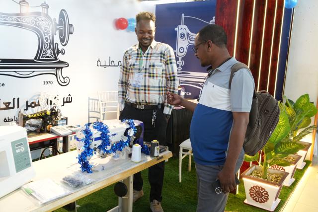 (260127) -- ATBARA, Jan. 27, 2026 (Xinhua) -- A sewing machine manufacturer introduces products to a visitor at the exhibition in Atbara, River Nile State, Sudan, Jan. 27, 2026. Atbara, a relatively stable city in northern Sudan's River Nile State, is hosting the "Made in River Nile" exhibition, which highlights Sudanese industry's resolve to aid economic recovery and revive national production, even amid the country's ongoing internal conflicts. (Photo by Fayez Elzaki/Xinhua)