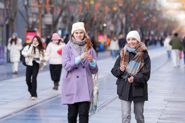 (260128) -- BEIJING, Jan. 28, 2026 (Xinhua) -- German tourists Martha (R) and Sofie taste Tanghulu, a popular Chinese winter snack of crispy sugar-coated hawthorns, at Qianmen Street in Beijing, capital of China, Jan. 7, 2026.
  Fueled by China's expanding visa-free policies, inbound travel surged in 2025, with visa-free entries jumping 49.5 percent year-on-year to nearly 30.1 million, official data showed.
  The National Immigration Administration said on Wednesday that international visitors made over 82 million crossings in total, marking a 26.4 percent year-on-year increase.
  Currently, China offers visa-free entry to citizens of 76 countries. Plus, travelers from 55 countries can take advantage of a 240-hour visa-free transit policy at 65 different entry points. 
  Beyond short-term visits, this openness is fostering a vibrant community of international residents. More scholars, students, and professionals are choosing to live and work in China, deepening people-to-people bonds. China, with much to be explored and a lot more to offer, continues to captivate hearts and minds worldwide. (Xinhua/Ju Huanzong)