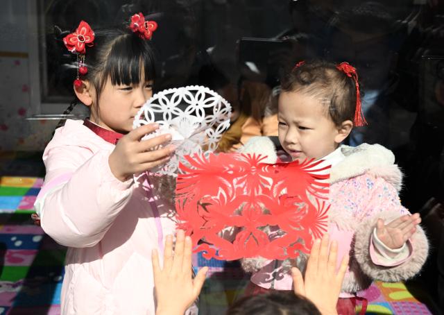 (260204) -- HOHHOT, Feb. 4, 2026 (Xinhua) -- Two children paste paper-cutting works on a window in Taigedou Village of Horinger County, north China's Inner Mongolia Autonomous Region, Feb. 4, 2026. Events featuring the traditional craft of Horinger paper-cutting, a national intangible cultural heritage, were held in Horinger County on Wednesday to mark "Lichun," or the Beginning of Spring, the first of the 24 solar terms on the Chinese lunar calendar, and to welcome the upcoming Spring Festival. (Xinhua/Bei He)