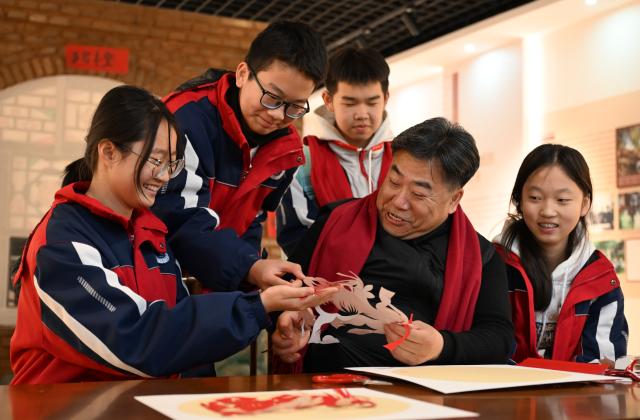 (260204) -- HOHHOT, Feb. 4, 2026 (Xinhua) -- Duan Jianjun (front, 2nd R), a national representative inheritor of Horinger paper-cutting, displays paper-cutting skills for students at an exhibition hall of the Horinger Tuchengzi Archaeological Site Park in Horinger County, north China's Inner Mongolia Autonomous Region, Feb. 4, 2026. Events featuring the traditional craft of Horinger paper-cutting, a national intangible cultural heritage, were held in Horinger County on Wednesday to mark "Lichun," or the Beginning of Spring, the first of the 24 solar terms on the Chinese lunar calendar, and to welcome the upcoming Spring Festival. (Xinhua/Bei He)
