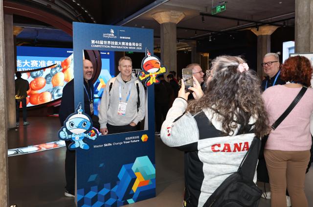 (260205) -- SHANGHAI, Feb. 5, 2026 (Xinhua) -- Guests pose for a photo in front of the exhibition board of the 48th WorldSkills Competition Preparation Week at WorldSkills Museum in Shanghai, east China, Feb. 4, 2026. As one of the 48th WorldSkills Competition Preparation Week activities, the Shanghai promotion campaign and intangible cultural heritage experience event was held here on Wednesday, which was attended by over 700 guests from home and abroad. (Xinhua/Fang Zhe)