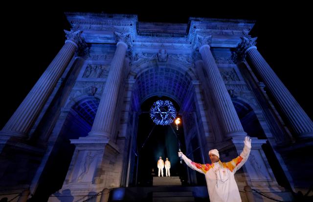 (260207) -- MILAN, Feb. 7, 2026 (Xinhua) -- Torchbearers Enrico Fabris (front) passes the Olympic flame during the opening ceremony of the Milan-Cortina 2026 Olympic Winter Games at the Arco della Pace in Milan, Italy, Feb. 6, 2026. (Jamie Squire/Pool via Xinhua)