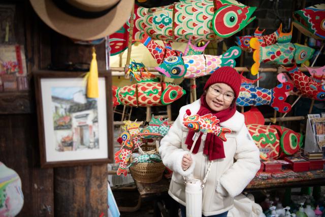 (260208) -- YIXIAN, Feb. 8, 2026 (Xinhua) -- A girl poses for photos at a fish lantern workshop in Bishan Village of Yixian County, east China's Anhui Province, Feb. 7, 2026.
  Ancient villages in Yixian County are filled with festive vibe as the Spring Festival approaches. Locals follow folk customs by making steamed rice cakes, fish lanterns, and writing spring couplets, drawing tourists to share the festive joy together. (Xinhua/Zhang Duan)