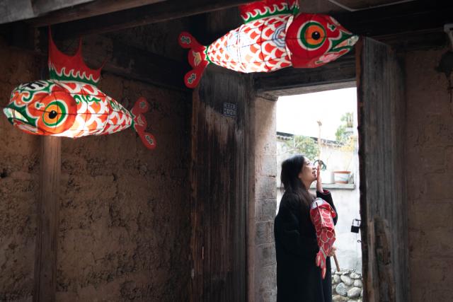 (260208) -- YIXIAN, Feb. 8, 2026 (Xinhua) -- A tourist poses for photos with a fish lantern in Bishan Village of Yixian County, east China's Anhui Province, Feb. 7, 2026.
  Ancient villages in Yixian County are filled with festive vibe as the Spring Festival approaches. Locals follow folk customs by making steamed rice cakes, fish lanterns, and writing spring couplets, drawing tourists to share the festive joy together. (Xinhua/Zhang Duan)