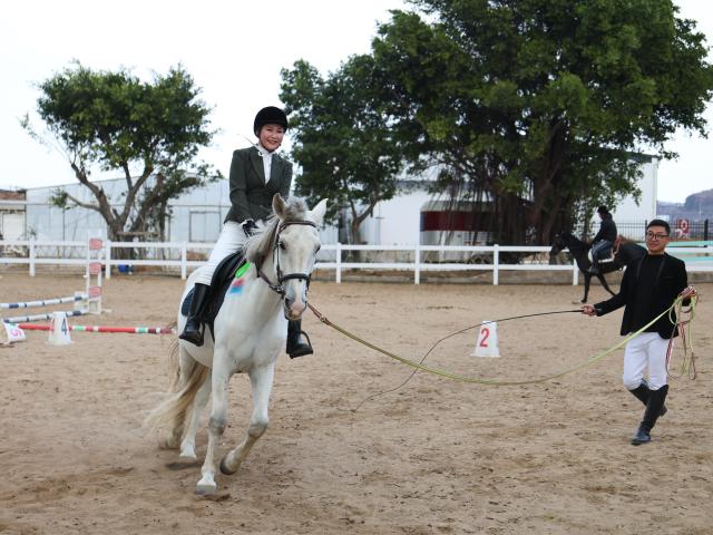 (260208) -- XIAPU, Feb. 8, 2026 (Xinhua) -- A woman learns horse riding under the guidance of a staff member (R) at a racecourse of a cultural and creative base in Xiapu County, southeast China's Fujian Province, Feb. 7, 2026. Horse-themed tourism has surged recently in Xiapu County as the lunar Year of the Horse approaches. (Xinhua/Jiang Kehong)