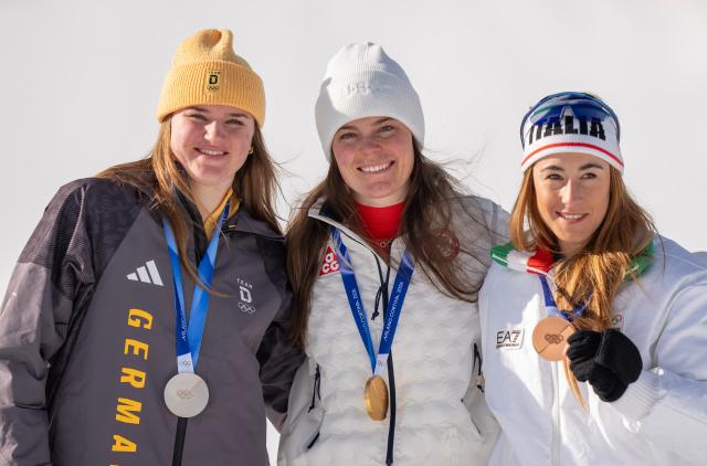(260208) -- CORTINA D'AMPEZZO, Feb. 8, 2026 (Xinhua) -- Gold medalist Breezy Johnson (C) of the United States, silver medalist Emma Aicher (L) of Germany and bronze medalist Sofia Goggia of Italy pose for a group photo during the awarding ceremony of the alpine skiing women's downhill at the Milan-Cortina 2026 Olympic Winter Games in Cortina, Italy, Feb. 8, 2026. (Xinhua/Fei Maohua)