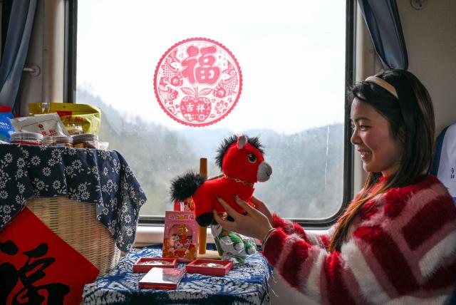 (260209) -- KAILI, Feb. 9, 2026 (Xinhua) -- A passenger looks at a plush toy horse on the train No. 5640 in southwest China's Guizhou Province on Feb. 8, 2026. The train No. 5640 runs in Guizhou Province between Yuping Dong Autonomous County of Tongren City and provincial capital Guiyang City. It connects more than 100 ethnic minority villages along the route and makes travel more convenient for the villagers.
   A New Year market has been introduced on the train No. 5640 upon the upcoming Chinese New Year, during which fresh agricultural products and folk customs were displayed for passengers along the way. (Xinhua/Yang Wenbin)