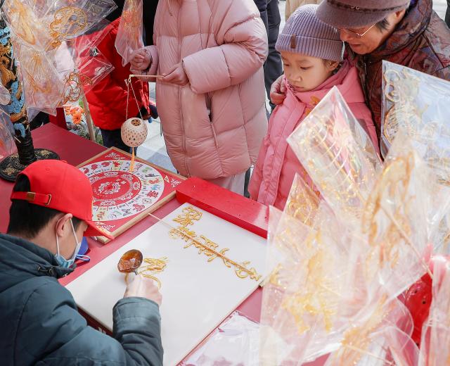 (260210) -- BEIJING, Feb. 10, 2026 (Xinhua) -- A child waits for a sugar painting at a Spring Festival market of Longfusi commercial area in Dongcheng District of Beijing, capital of China, on Feb. 10, 2026. As the Spring Festival approaches, the Longfusi commercial area is filled with festive atmosphere, attracting a large number of citizens and tourists to visit here. (Xinhua/Chang Nengjia)
