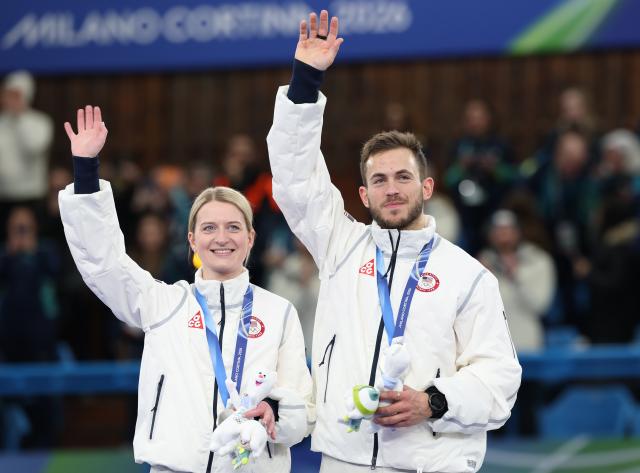 (260210) -- CORTINA D'AMPEZZO, Feb. 10, 2026 (Xinhua) -- Cory Thiesse (L) and Korey Dropkin of the United States wave during the awarding ceremony of the curling mixed doubles at the Milan-Cortina 2026 Olympic Winter Games in Cortina, Italy, Feb. 10, 2026. (Xinhua/Ding Xu)