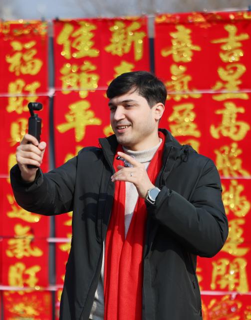 (260211) -- TIANJIN, Feb. 11, 2026 (Xinhua) -- Suleimanov Umar films a video at a festive fair in Chuanfangyu Town of Jizhou District, north China's Tianjin, Feb. 10, 2026. On the occasion of traditional Chinese Xiaonian Festival in northern China, which fell on Tuesday this year, Suleimanov Umar, a 26-year-old Tajikistan student in Nankai University of Tianjin, and other international students visited a local festive fair in Chuanfangyu Town to experience the vibrant traditions of Chinese New Year. Celebrated on the 23rd day of the last month of the Chinese lunar calendar, Xiaonian is a festival marking the start of the countdown to the Chinese New Year.
   When Suleimanov was a child, most neighbors were Chinese working in Tajikistan, thus he was deeply impressed by Chinese New Year traditions such as putting up Spring Festival couplets and making dumplings.
   When in middle school, he began studying Chinese at local Confucius Institute, and then chose to go to university in China with the support of his family. While staying in China he immersed himself in social practice and actively participated in cultural exchange activities.
    Speaking of the future, Suleimanov said, "I hope I could engage in diplomatic work after graduation and strive to become an envoy of friendship". (Xinhua/Li Ran)