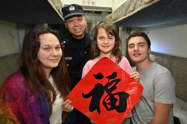 (260211) -- NANNING, Feb. 11, 2026 (Xinhua) -- Huang Qingming gives a Chinese character "Fu"  (meaning good fortune) to foreign passengers on the train No. T8701 in south China's Guangxi Zhuang Autonomous Region, Feb. 10, 2026. The China-Vietnam international passenger rail service, which resumed operations on May 25, 2025, is now facing its first Spring Festival travel rush. Huang Qingming, a 58-year-old railway police officer, has been working on this route since 2012, responsible for the Nanning-Pingxiang section of trains No. T8701 and No. T8702 in Guangxi. 
   As a railway police officer, handling various emergencies, conducting train's security check and ensuring passenger safety during the journey are part of Huang's daily routine.
   Approaching retirement, Huang cherishes his role deeply, "Serving as a railway police officer on the China-Vietnam international passenger rail service, safeguarding the trains' security and passengers' safety, has been an honorable and unforgettable experience in my career." (Xinhua/Lu Boan)